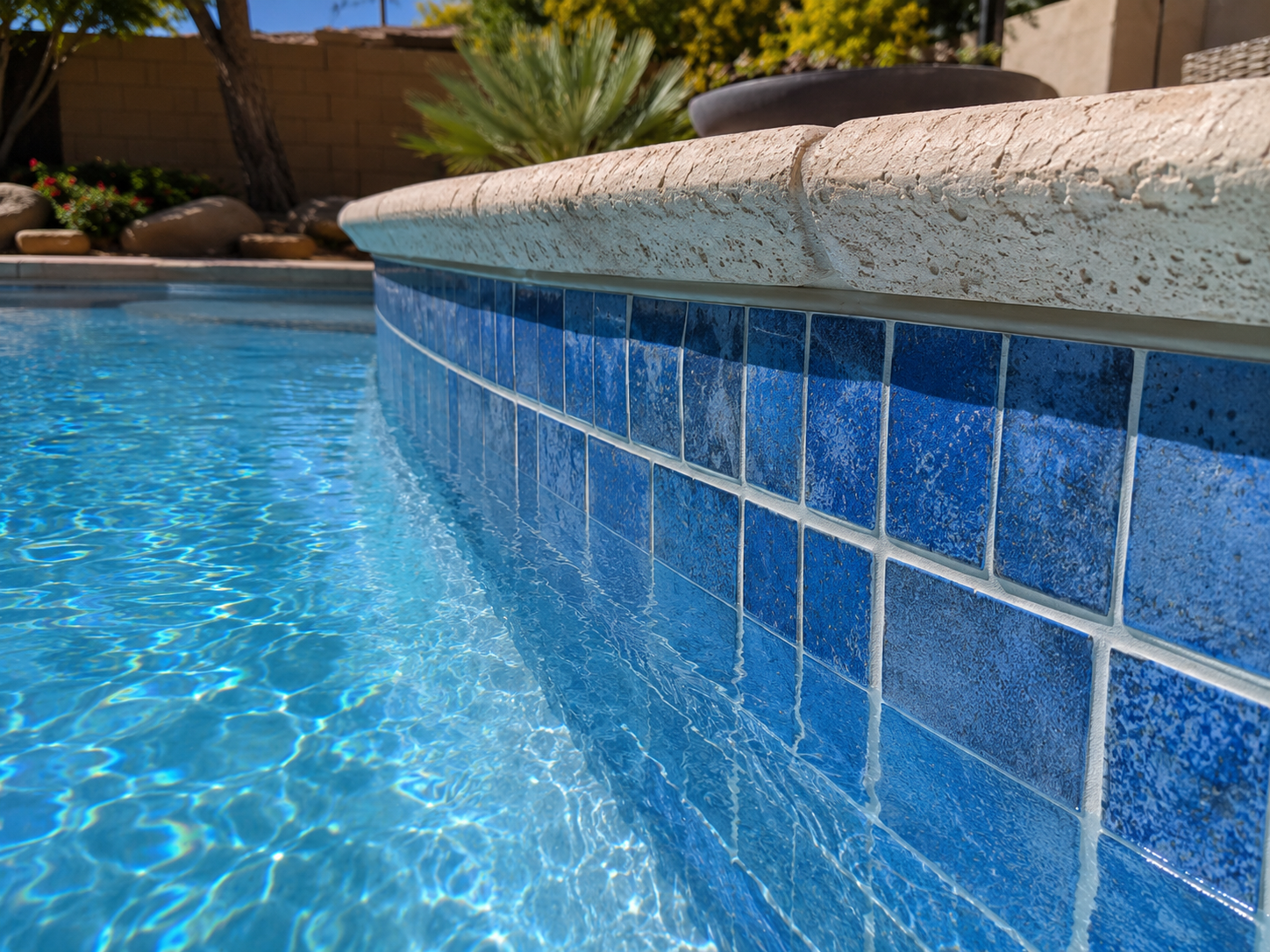 Close-up of a pool edge with blue tile coping and shimmering water along a curved wall.